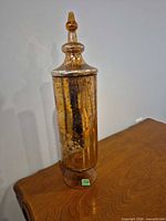 Full view of copper-tone glass jar with lid on table