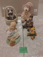 Group shot of five visible porcelain figurines including basket with Siamese cats, teddy bear, seated girl, rabbit, orange cat