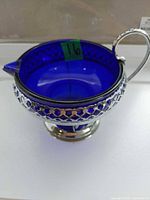 Oblique view showing blue glass insert, silver-tone lattice holder, handle and spout