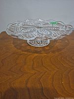 Side view of clear pressed glass pedestal dish on wooden surface
