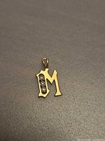 Front view of gold M pendant showing diamonds and bail