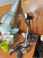 Silver adjustable swing-arm desk lamp with cord; black lamp partially visible; shows surface condition