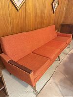 Full view of orange mid-century sofa against wood panel wall