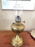 Full view of brass kerosene lamp showing pedestal base, fuel font, burner, chimney