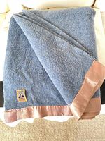 Folded blue wool blanket showing pink satin trim and overall texture