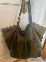Front view of olive faux-leather tote hanging, showing overall shape and exterior pocket