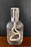 Front view of clear glass Lampe Berger lamp showing etched design, wick, and silver vented cap