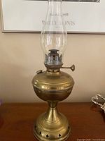 Full view of brass kerosene lamp standing on pedestal base with clear glass chimney attached