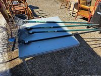 Four metal fan rakes laid on folding table showing full length handles and heads