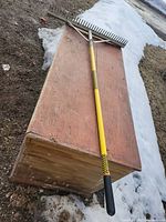 Full view of rake on wooden surface and snow backdrop