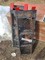 Two folded steel mesh ramps with red end caps leaning against surface