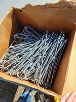 Open cardboard box filled with numerous metal hooks