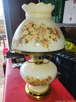 Full view of vintage milk glass hurricane lamp showing shade, base, floral design and brass-tone hardware