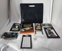 Full kit layout showing carry case, novel, booklets, cards, score pad and die