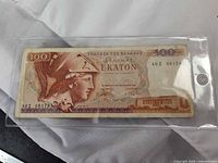 Obverse of Greek 100 drachmai note in plastic sleeve showing Athena profile