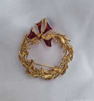 Front view of gold-tone wreath brooch with red enamel bow