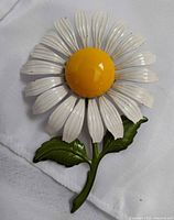Front view of enamel daisy brooch showing petals, center, stem, leaves