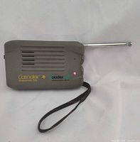 Front view showing speaker grille, logos, LED, antenna extended, wrist strap visible