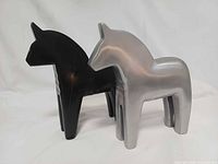 front angled view of both black wooden and silver aluminum Dala horse figurines