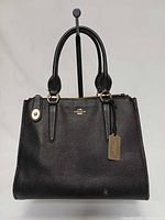 Front view of black Coach Crosby carryall tote showing logo, hangtag and handles