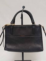Front view of black pebbled leather Coach Mini Borough handbag showing logo, rolled handles and strap attachment