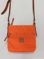 Front view showing monogram pattern, logo patch, front zipper pocket, strap attachment