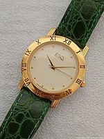 Front view showing gold-tone case, Roman numeral bezel, white dial, green strap