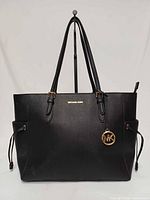 Front view of black Michael Kors tote with straps, logo, charm