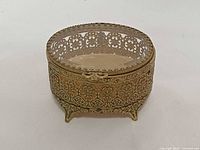 Front angled view showing oval shape, filigree sides, glass lid, footed base
