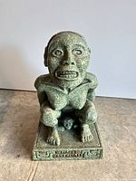 Front view of green speckled Aztec-style crouching figure statue on decorated base