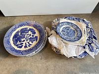 Stack of blue scenic dinner plates alongside wrapped smaller plates and platter