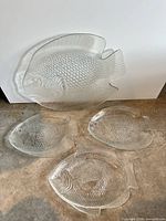 All four clear glass fish-shaped plates displayed together