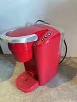 Front-side view of red Keurig machine showing drip tray, handle, control buttons, power cord
