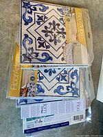 Stack of four sealed packs of FloorAdorn vinyl floor tiles displaying pattern and labeling