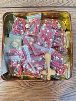 Tin containing multiple bagged red bead rosaries, wooden cross, metal icon