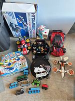 Overview of all toys spread on floor including boxed kit, vehicles, trains, board game