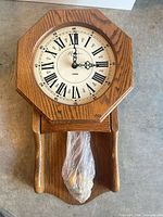 Front view of complete wall clock showing octagonal dial section, lower pendulum compartment, plastic-wrapped pendulum