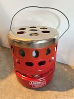 Full view of red catalytic heater with handle and perforated top