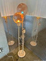 Full view of floor lamp showing base, off-white poles, two acrylic globe shades illuminated