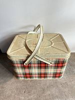Angled view showing entire plaid metal picnic basket, cream lid and handles