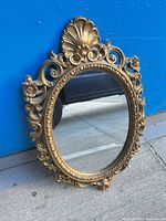Full view of gold ornate oval mirror against wall