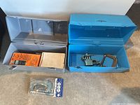 Open grey and blue Thermos tool boxes showing lids and bases with clamps, vise, packaged items