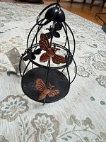 Front view of black wire bird cage with bee accents, tag visible