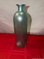 Full view of blue-green glass bottle vase on red surface