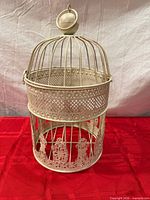 Front view of cream metal bird cage showing lattice and floral cut-outs