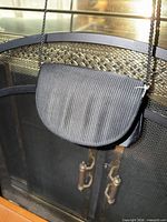 Front of black satin purse hanging, showing ribbed flap and strap