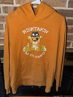 Full view of burnt orange hoodie on hanger showing front graphic and pocket