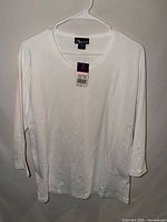 Front view of white 3/4 sleeve T-shirt on hanger showing overall design