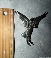 Front view of silver-tone angel brooch beside ruler showing length