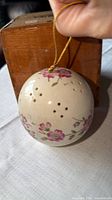 Full view of ceramic sphere showing floral design, vent holes, and hanging cord